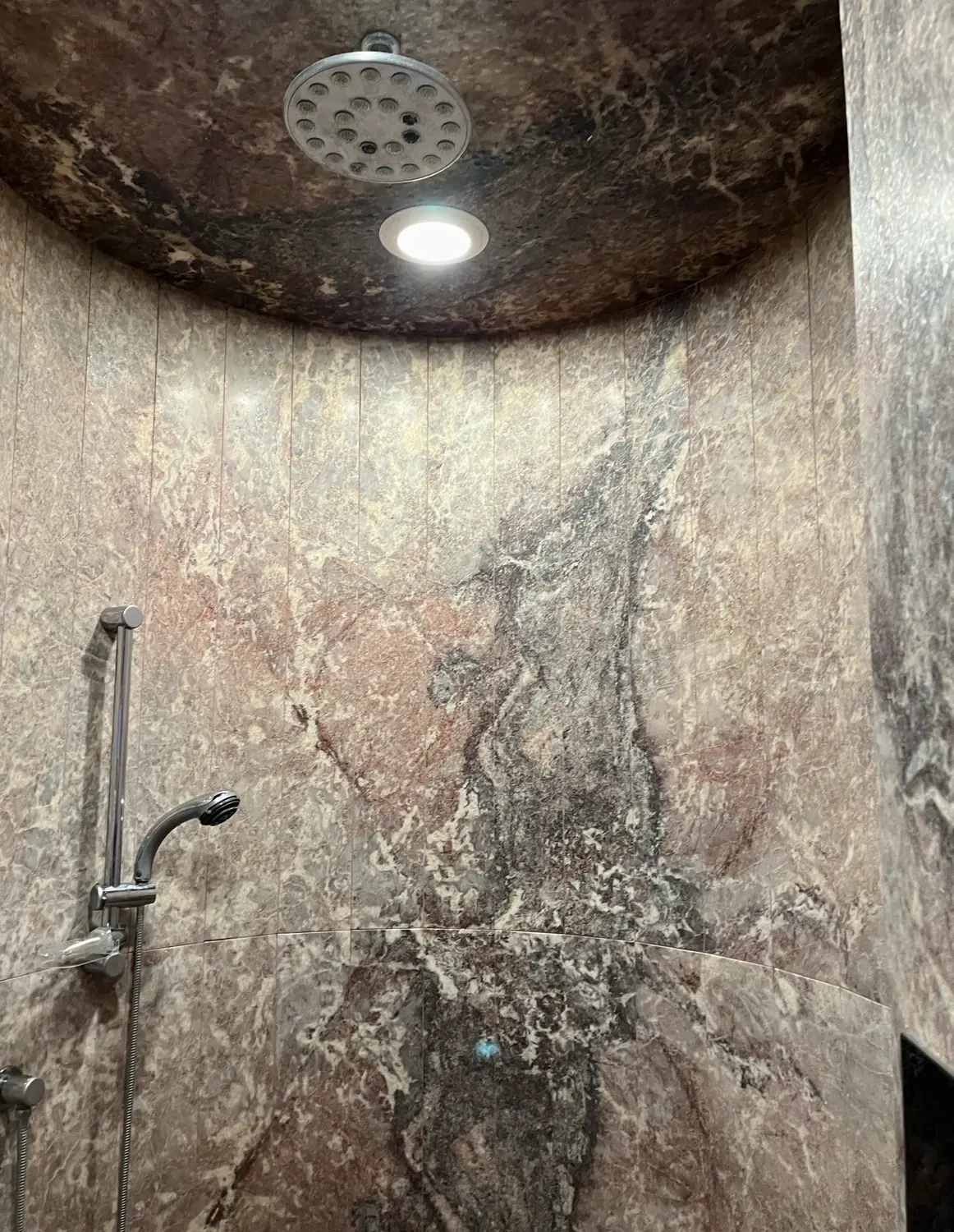 Rounded shower enclosure clad in veined stone with a domed stone ceiling
