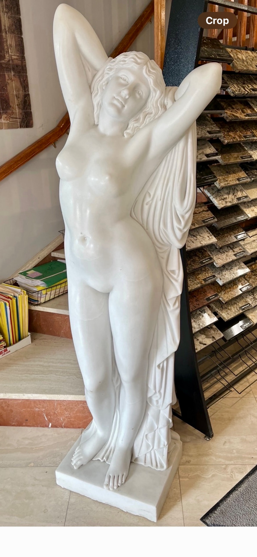 White marble statue of a classical female figure beside stone sample racks