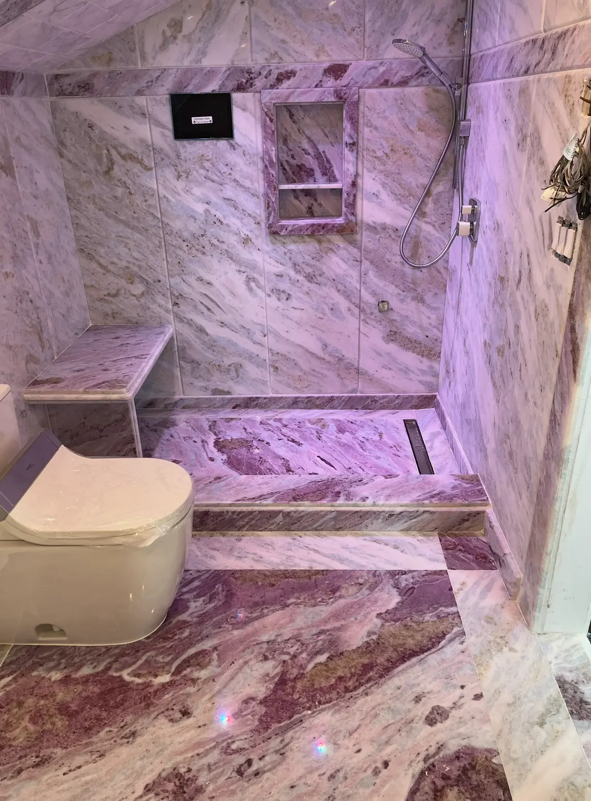 Walk-in shower fully clad in violet-veined marble with stone bench
