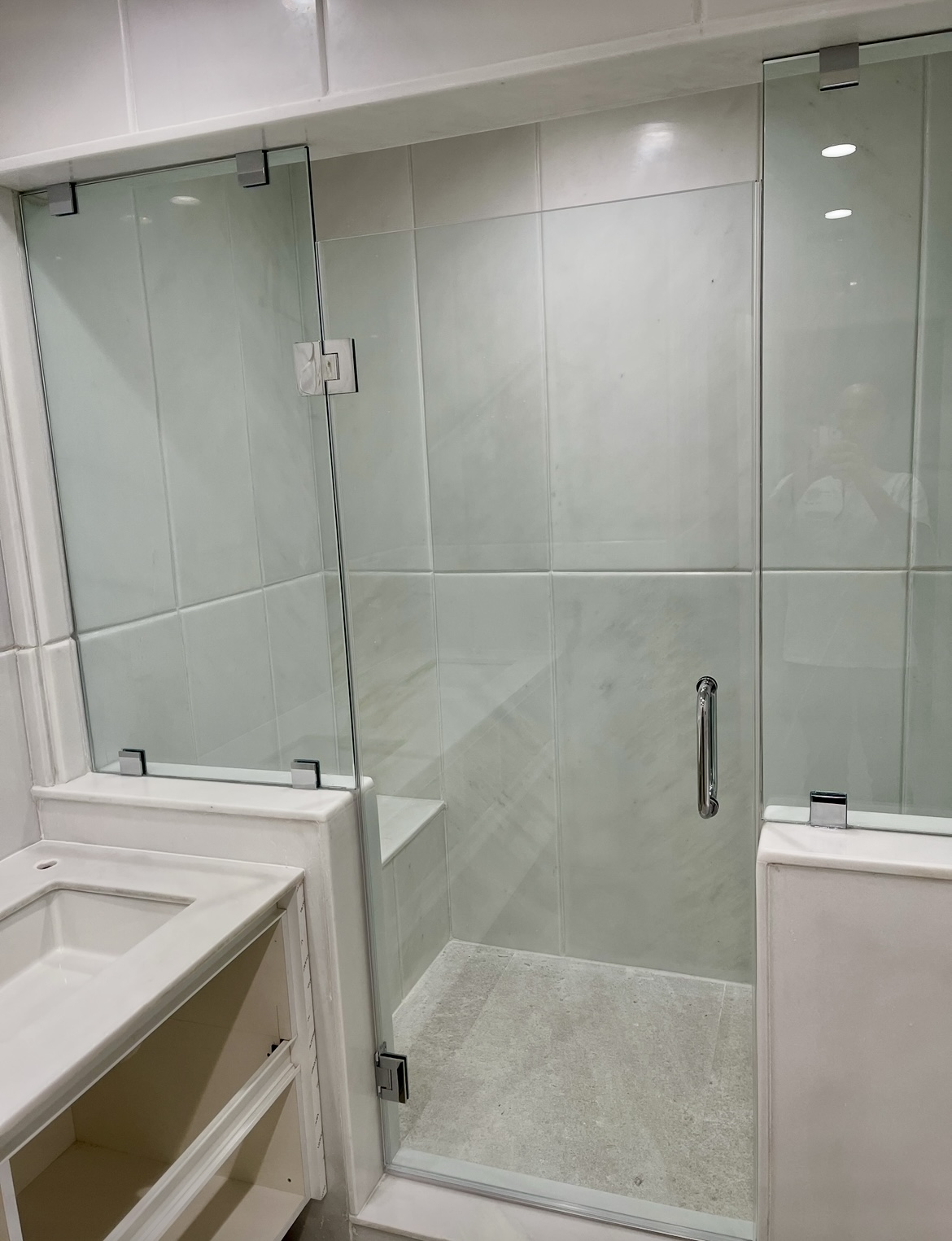 White marble shower enclosure with frameless glass door and bench