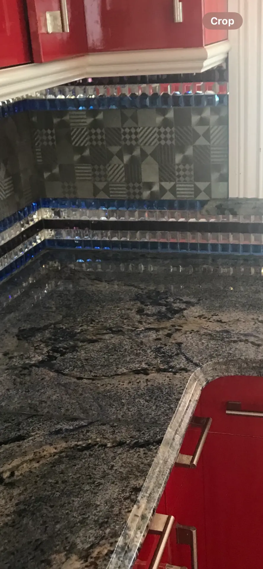 Dark veined granite kitchen countertop with red cabinetry and mosaic tile backsplash