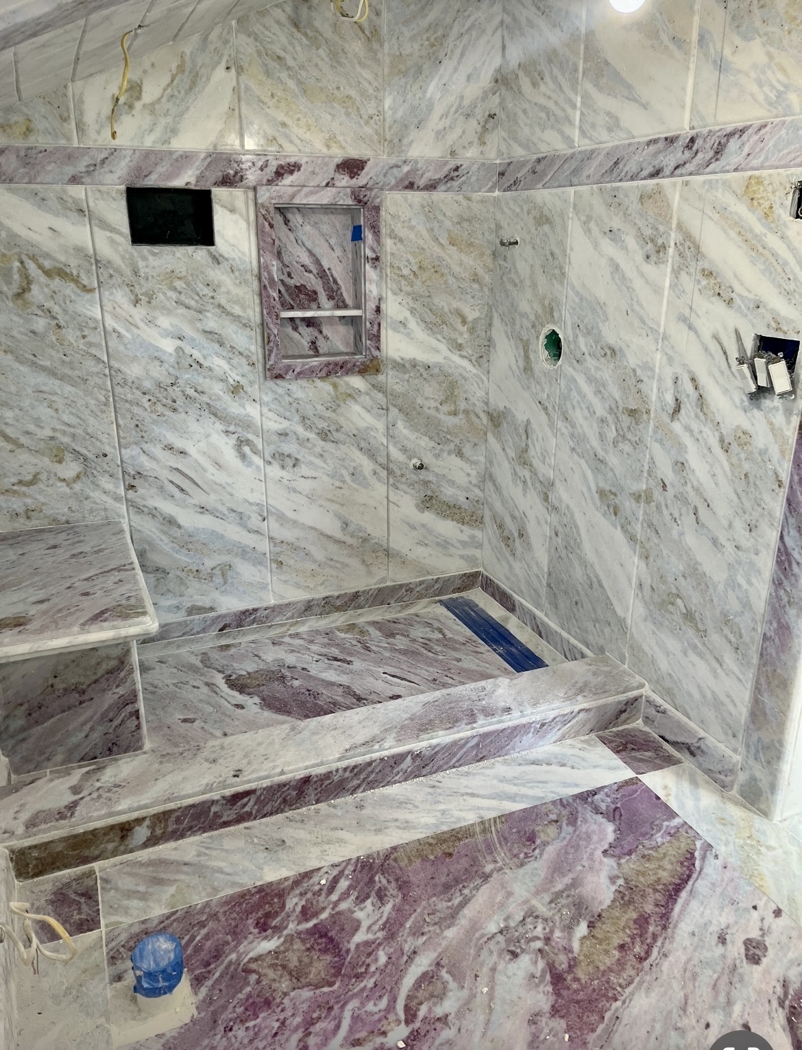 Marble shower enclosure with violet-veined stone walls, bench and curb
