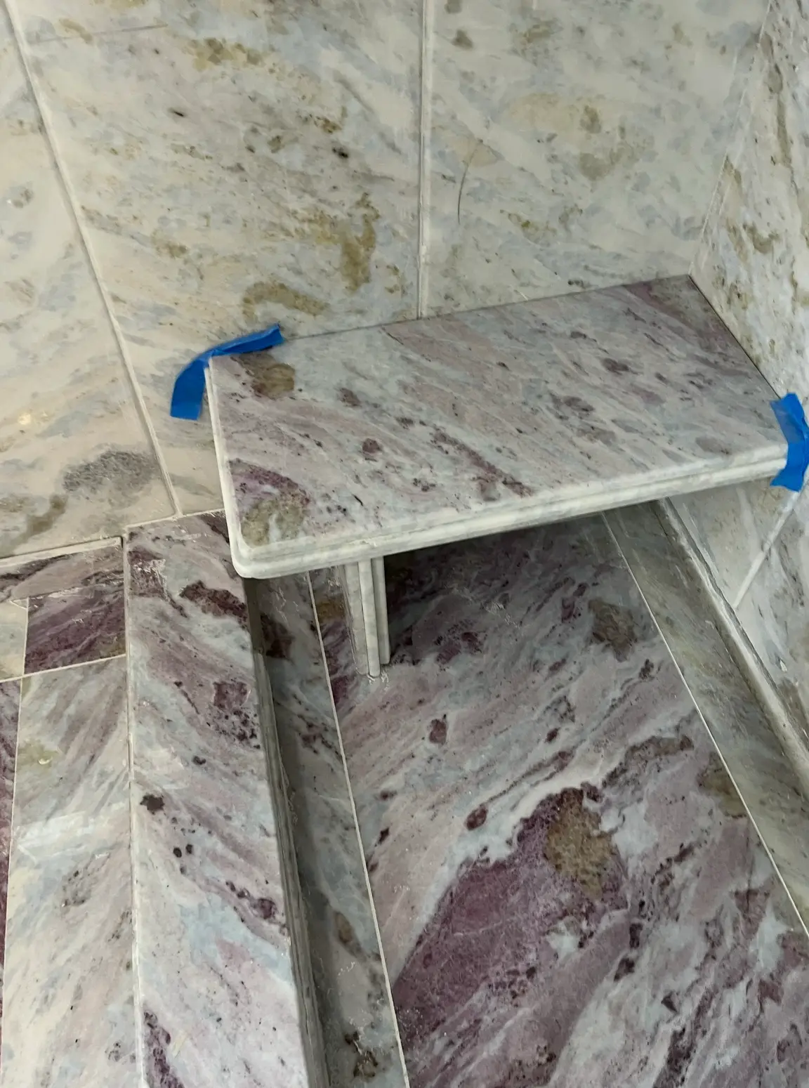Marble shower bench mounted in a stone-tiled shower corner