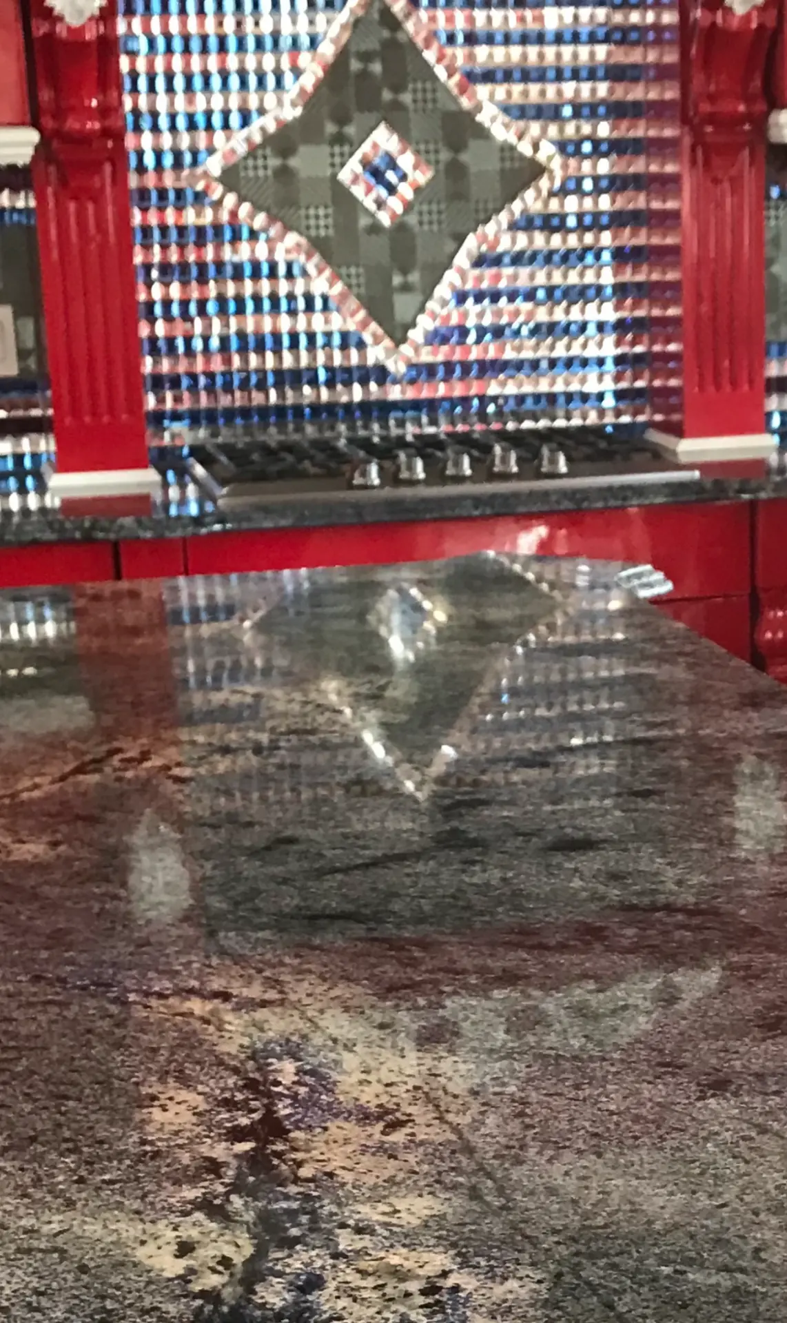 Polished granite kitchen countertop with red cabinetry and mosaic tile