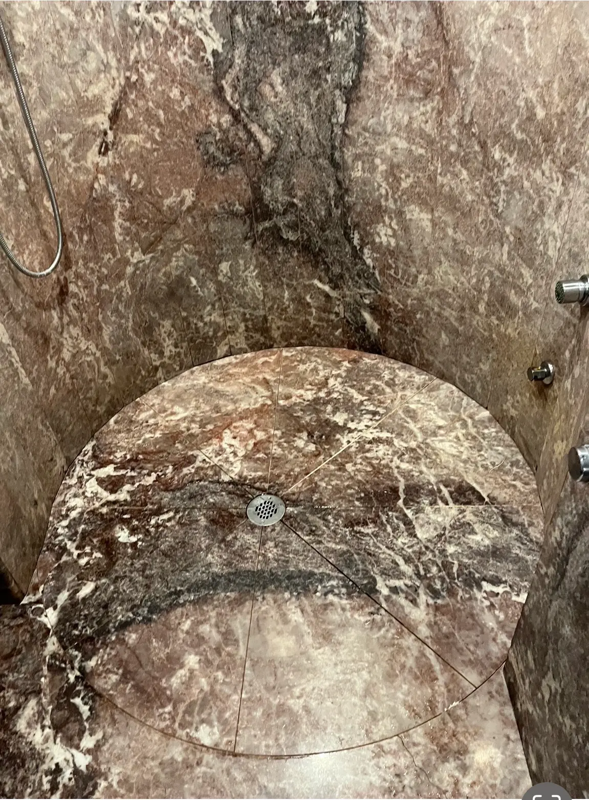 Curved shower floor cut from veined stone with radial seams to a center drain