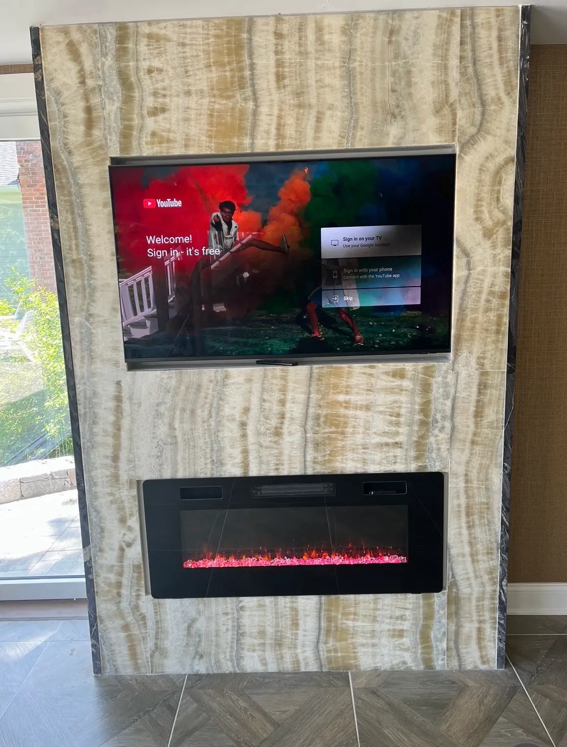 Floor-to-ceiling onyx feature wall with mounted TV and linear electric fireplace