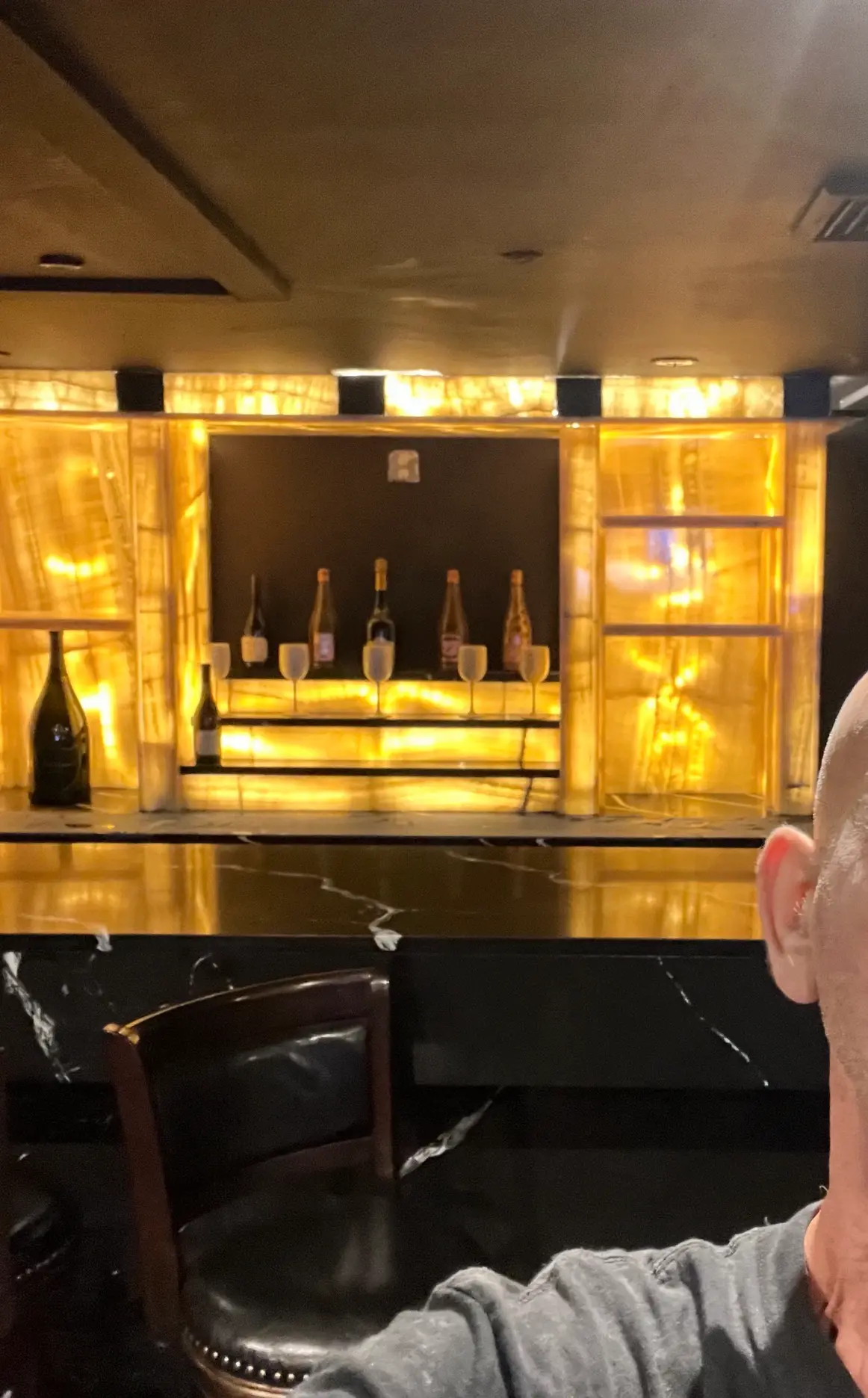 Home bar with glowing backlit onyx panels and polished black marble top